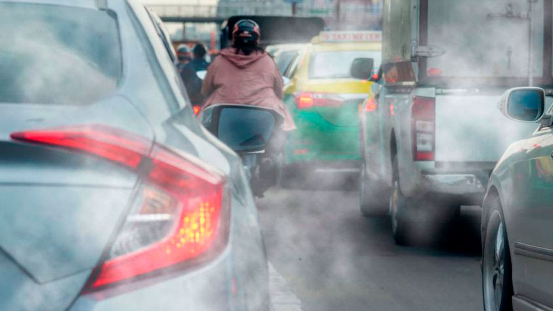 Coche expulsando humo blanco por el tubo de escape mientras circula por carretera debido a una posible avería del motor.